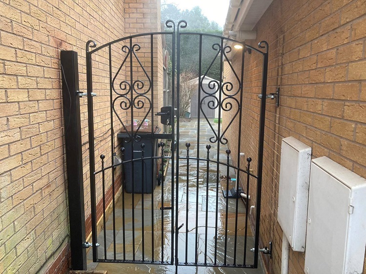 Arched top double metal gates fitted between brick walls